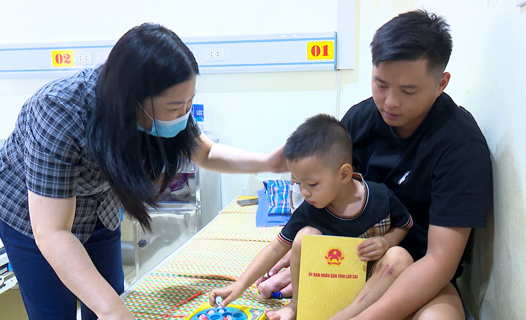 Đồng chí Vũ Thị Hiền Hạnh - Phó Chủ tịch UBND tỉnh tận tình thăm hỏi sức khỏe một cháu nhỏ đang điều trị tại Khoa Ngoại tổng hợp - Trung tâm Y tế khu vực Văn Yên. sequence-0100-04-54-17still013.jpg