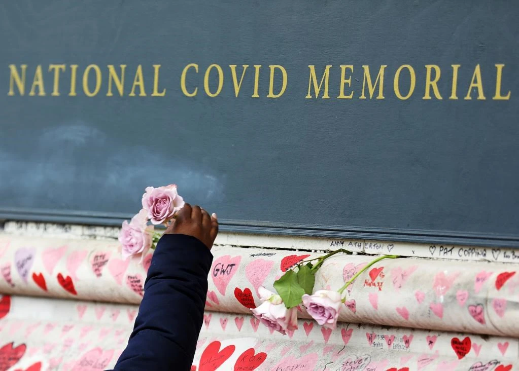 Một người phụ nữ cài hoa trên Bức tường tưởng niệm các các nạn nhân tử vong vì COVID -19 ở London, Anh, ngày 27/3/2022. (Ảnh: Xinhua)