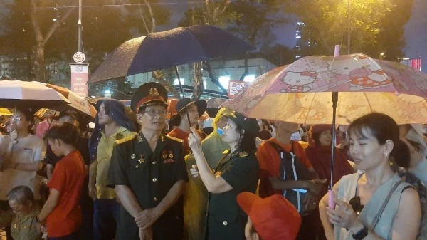 Gần đến giờ sơ duyệt diễu binh, diễu hành, trời bất ngờ đổ mưa lớn. Mặc dù cơn mưa khá nặng hạt, nhưng người dân vẫn đứng dưới mưa, che bằng áo khoác mỏng hoặc khăn trùm đầu,… kiên nhẫn chờ đợi xem diễu binh, diễu hành.