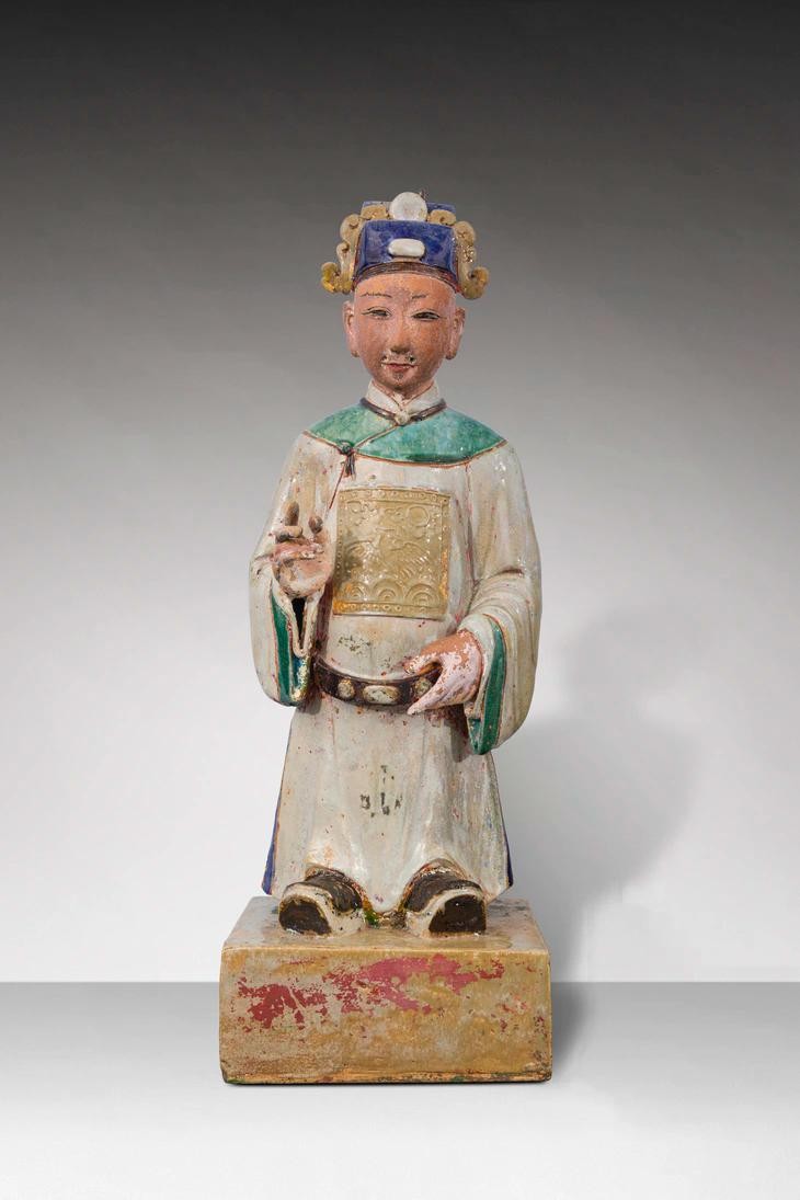 Tượng thị giả (người hầu) trong tư thế đứng trên bệ hình vuông, đầu đội mũ phốc vuông đắp nổi viên ngọc và mây. Mặt để mộc, dùng sơn để vẽ chân mày và mắt, tai to, trên mặt tạo 5 lỗ để gắn râu. Thân mặc áo dài màu trắng ngà, phần vai và ống tay áo màu xanh viền nâu, có đai, trên thân áo có “bổ tử” trang trí hình chim phượng, thủy ba, mây đối xứng trước và sau lưng. Tay trái cầm đai, tay phải đưa lên cao trước ngực trong tư thế cầm bút lông, chân mang hia.