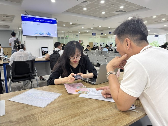 Los funcionarios del Centro de Servicios de Administración Pública guían a las personas para obtener números de cola en línea para registros relacionados con tierras a través de la aplicación iHanoi. Cán bộ Trung tâm phục vị hành chính công hướng dẫn người dân lấy số thứ tự online đối với hồ sơ liên quan đến đất đai qua ứng dụng iHanoi.