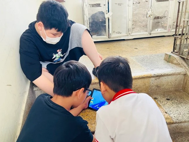 Học sinh một trường tiểu học tại Hà Nội túm tụm chơi game ngay cầu thang của trường trong giờ ra chơi.