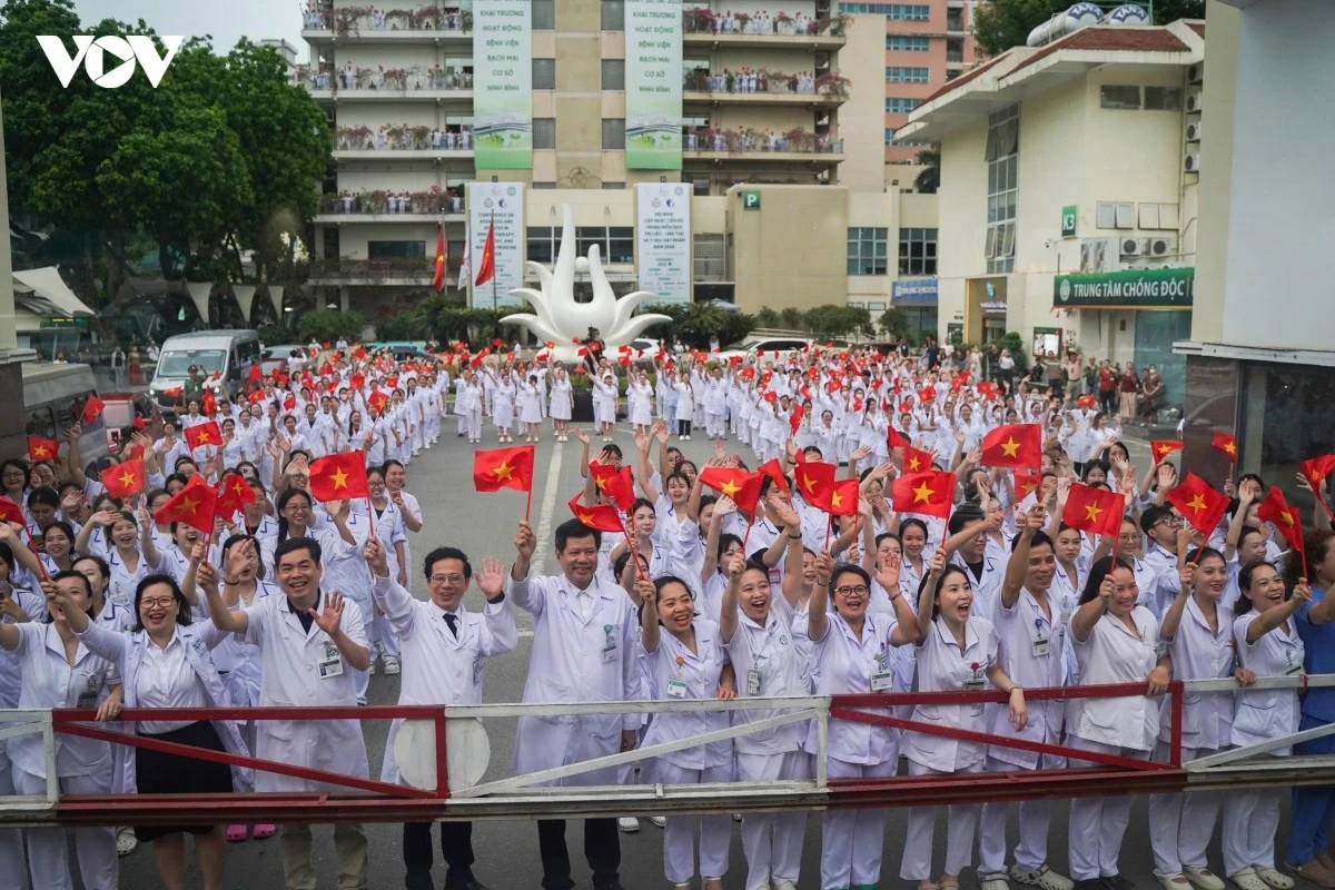 Các y bác sĩ tại cơ sở Hà Nội đứng thẳng hàng, trên tay là lá cờ đỏ sao vàng vẫy chào đoàn đi cơ sở Ninh Bình thực hiện nhiệm vụ khám chữa bệnh.