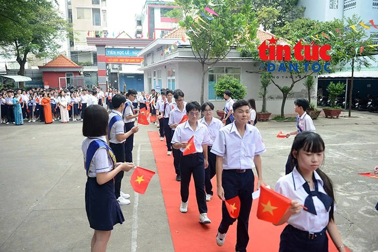 Các em học sinh tay cầm cờ Tổ quốc, háo hức tiến vào sân trường trong ngày khai giảng.