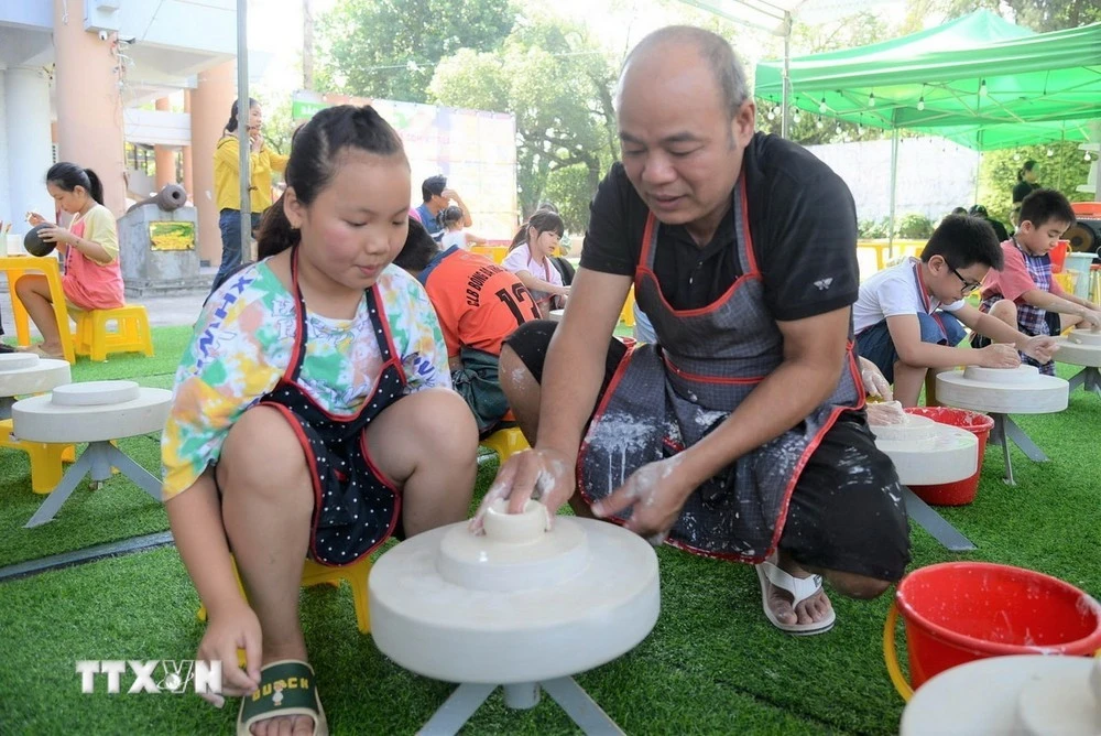 Nghệ nhân làm gốm hướng dẫn các du khách nhí vuốt, nặn gốm trên bàn xoay.