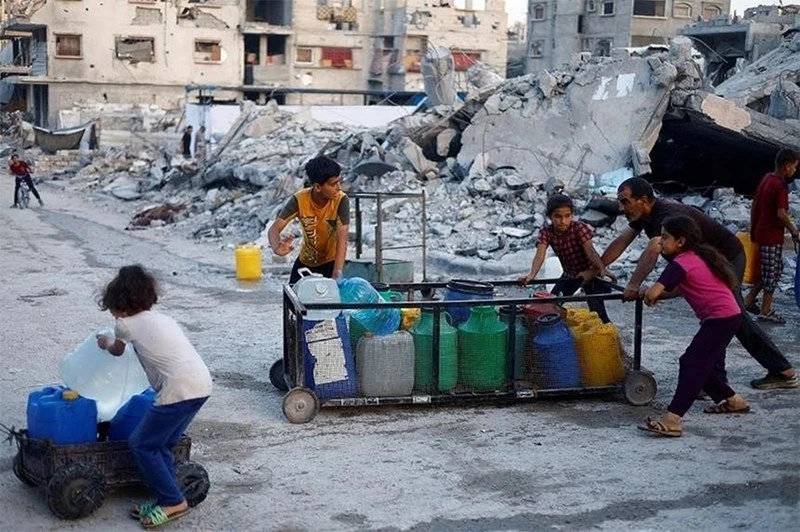 Một người đàn ông Palestine và trẻ em đẩy xe chở các thùng chứa nước ở Gaza.