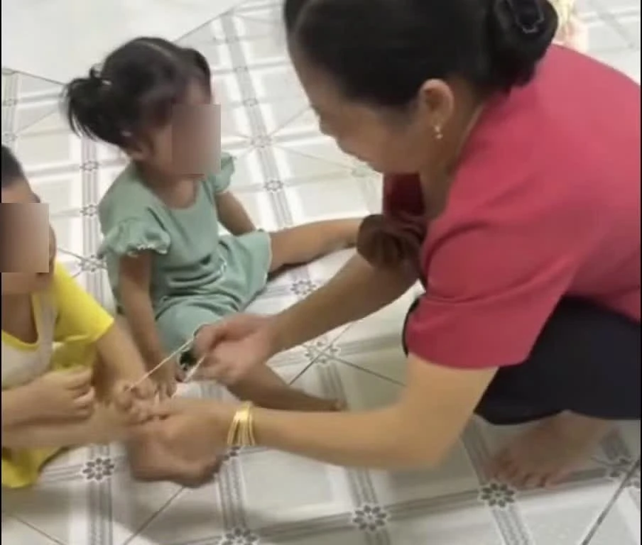 Nữ bảo mẫu dùng dây thun tác động vào chân trẻ. (Ảnh cắt từ clip).