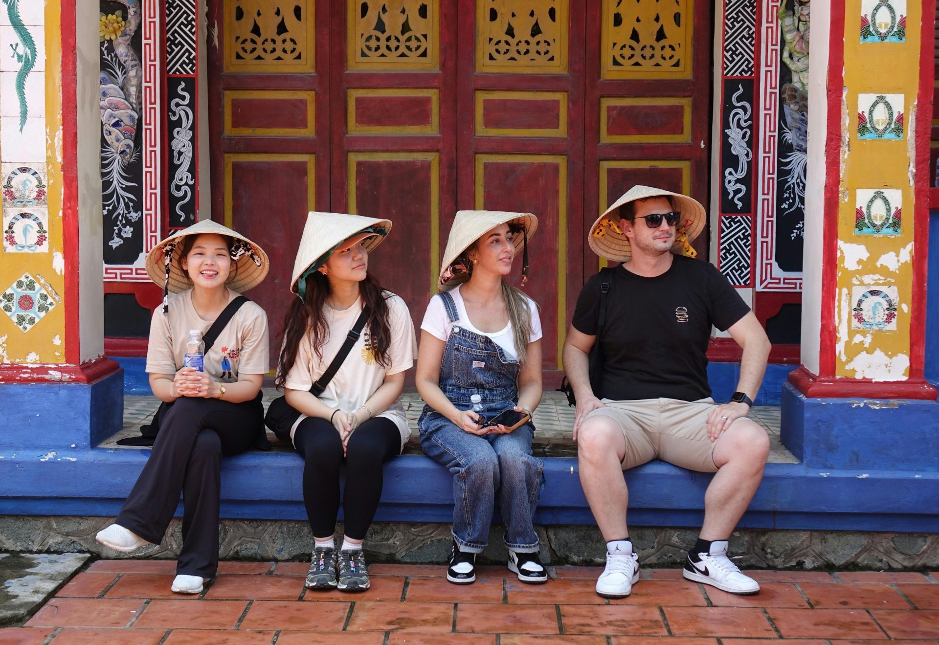 Nhóm du khách nước ngoài đội nón lá, thoải mái ngồi nghỉ chân tại một ngôi chùa.