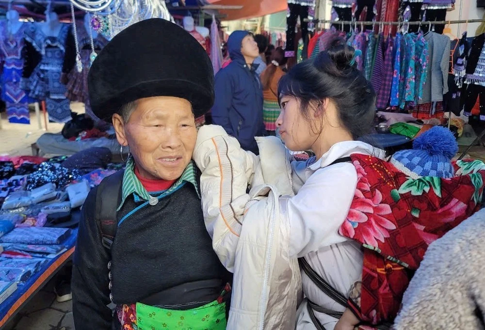 Một phụ nữ dân tộc đang được người cháu đeo khuyên tai mới mua tại chợ.