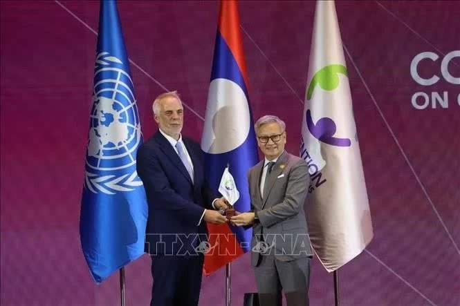 Đồng chí Thongsavanh Phomvihane trao cờ đăng cai Hội nghị Kiểm điểm lần thứ 4 Công ước Cấm bom, đạn chùm cho đại diện quốc gia chủ nhà tiếp theo. Ảnh: Xuân Tú/PV TTXVN tại Lào