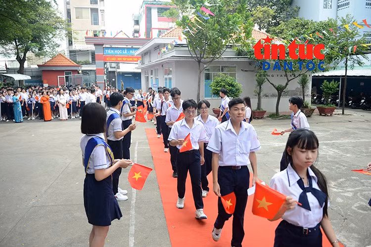 Các em học sinh tay cầm cờ Tổ quốc, háo hức tiến vào sân trường trong ngày khai giảng.