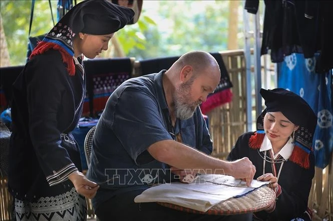 Du khách quốc tế trải nghiệm công đoạn vẽ họa tiết lên vải thổ cẩm bằng sáp ong.