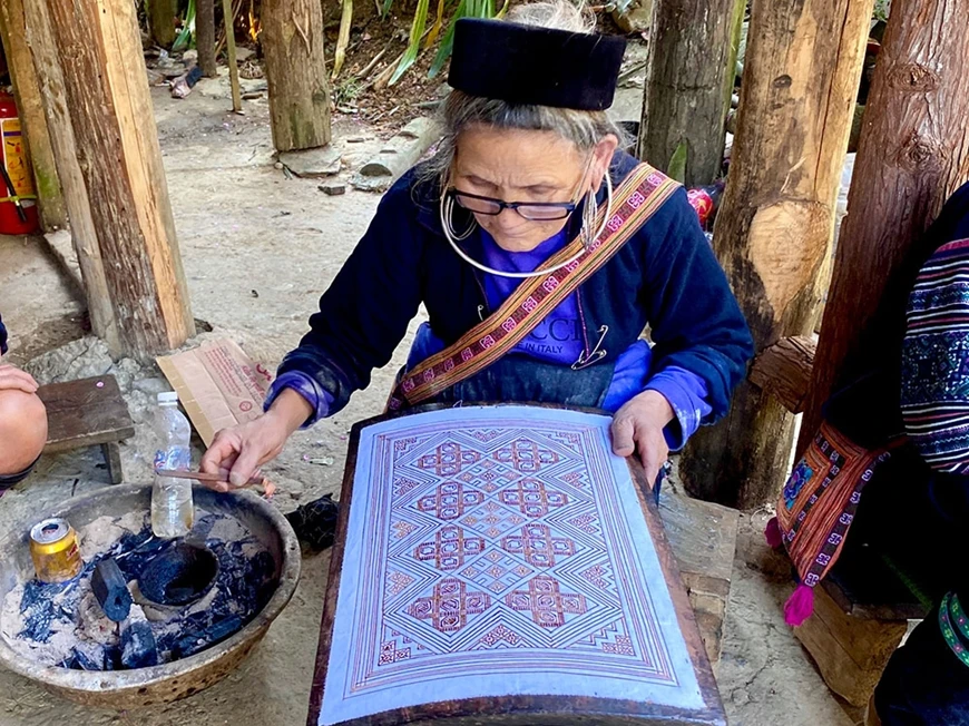 Bà Giàng Thị Dếnh đang thực hiện công đoạn dùng sáp ong vẽ lên nền vải trắng.