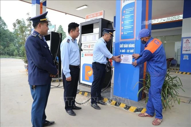 Cán bộ Đội Quản lý thị trường dán số 7 niêm yết số điện thoại đường dây nóng tại cửa hàng xăng dầu, tiếp nhận phản ánh của người dân.