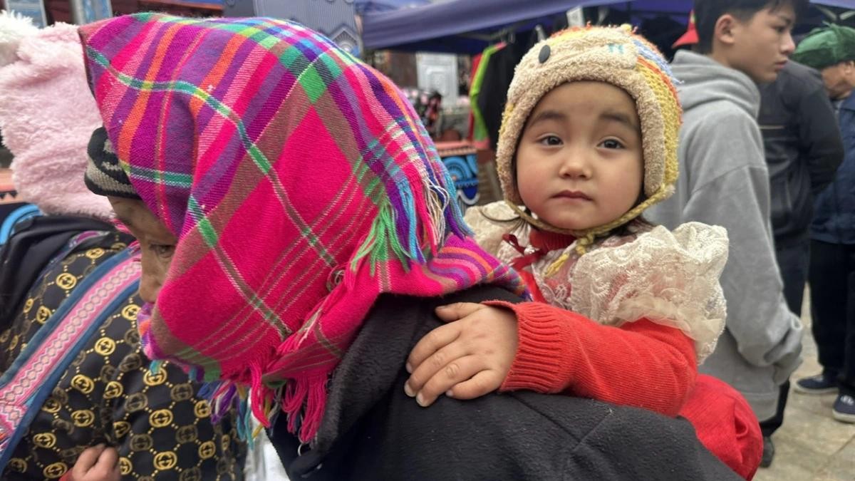 Một em bé được mẹ cõng trên lưng đi chợ Tết.