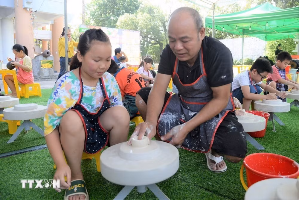 Nghệ nhân làm gốm hướng dẫn các du khách nhí vuốt, nặn gốm trên bàn xoay.